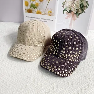Close-up of beige and brown corduroy baseball caps with gold rivet studs on textured surface