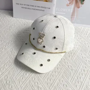 Detail of white jacquard baseball cap with gold bear charm and rhinestone chain