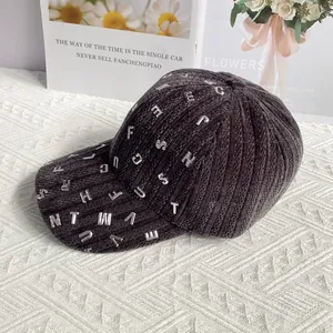 Dettaglio del cappellino in velluto a coste grigio scuro con lettere metalliche argentate