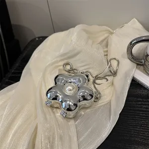 Silver flower crossbody mini bag with pearl detail and snake chain on white fabric