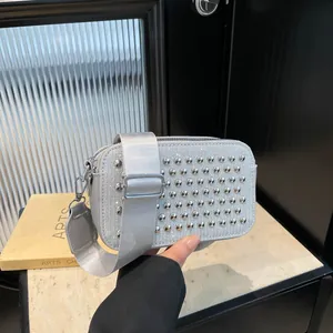 Silver square crossbody bag with sparkling rhinestones and metal rivets on stone surface