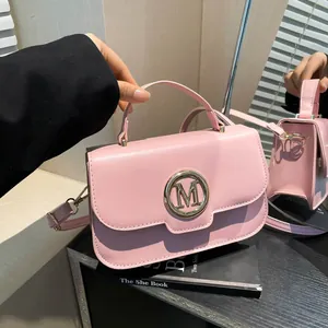 Roze PU-lederen handtas met gouden M-logo en schouderband op donkere achtergrond
