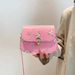 Sac bandoulière rose avec broderie florale et boucle dorée tenu par un modèle