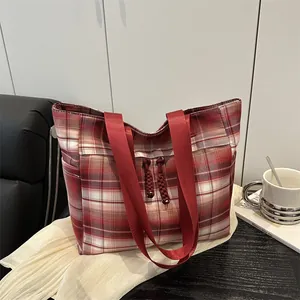 Sac fourre-tout à carreaux rouges avec larges anses et pompons sur fond boisé