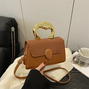 Brown woven crossbody bag with artistic gold metal handle on white silk background
