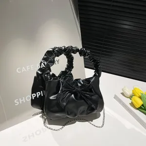 Chic black pleated handbag with bow detail and gold chain strap in a studio setting