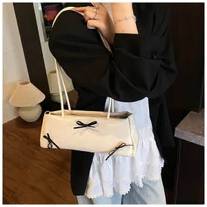 Detail of cream baguette bag with black bows worn under the arm with a blazer