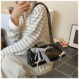 Detail of black glossy shoulder bag with white pearl bow and lace ribbons decoration