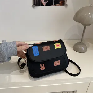 Sacoche noire en cuir avec écussons de dessins animés et bandoulière réglable