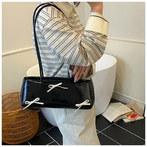 Detail of black glossy shoulder bag featuring three white decorative bows and thin straps