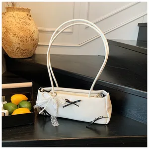 Detail of white leather shoulder bag with decorative pearl and lace bow on wooden stairs