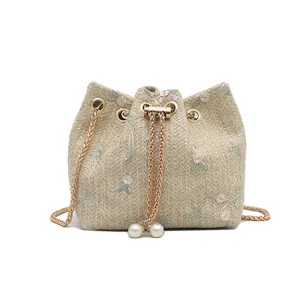 Woven straw bucket bag with floral embroidery, drawstring closure, and pearl accents