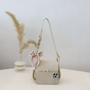 Minimalist cream shoulder bag with silk scarf accent and decorative pom-pom detail