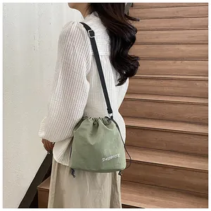 Detail of green nylon drawstring crossbody bucket bag showing fashion embroidery and strap