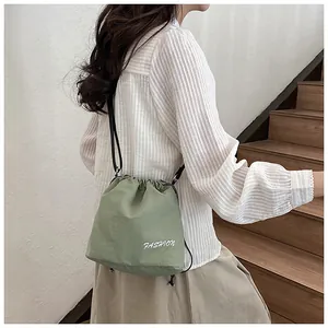 Detail of green drawstring nylon bucket bag with white embroidery on striped shirt