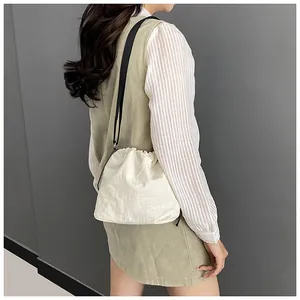 Detail view of cream drawstring crossbody bag featuring white fashion logo print