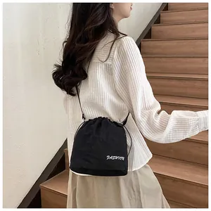 Detail of black nylon drawstring bucket bag with white Fashion embroidery on shoulder