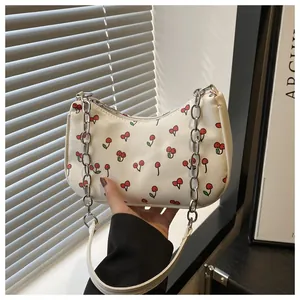 Detail of white half-moon bag with red cherry print and silver chain strap
