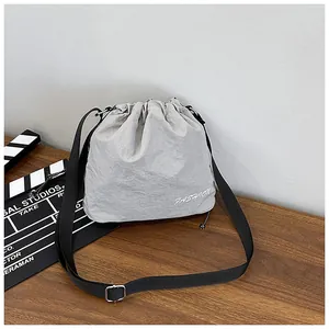 Detail of light gray nylon drawstring bucket bag with FASHION logo and adjustable strap
