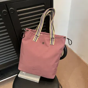 Large rose pink canvas tote bag with striped handles on a chair in a minimalist room