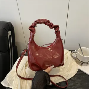 Dark red glossy handbag with scrunched handle on a white fabric background