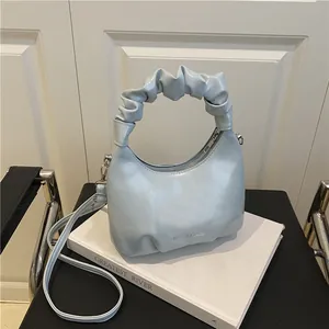 Silver metallic cloud handbag with ruched handle on a book in minimalist setting