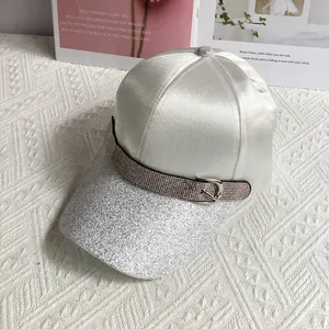 Detailed close-up of a silver satin baseball cap featuring glitter brim and rhinestone buckle