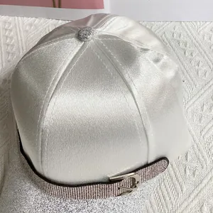 Detail of white satin baseball cap with rhinestone buckle strap and glitter finish