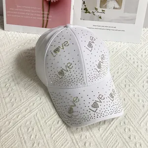Détail d'une casquette en coton blanc avec strass colorés formant Love sur fond blanc tricoté