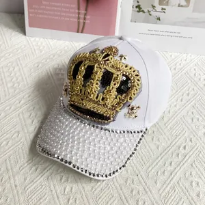 Close-up of white baseball cap with golden crown sequins, pearls, and rhinestone details