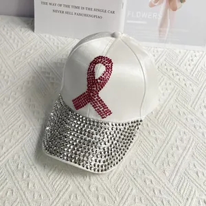 Detail of pink rhinestone ribbon logo and silver studded brim on white satin baseball cap