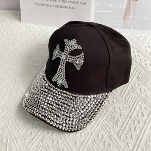 Close-up of a black denim baseball cap featuring a large rhinestone cross and studded brim