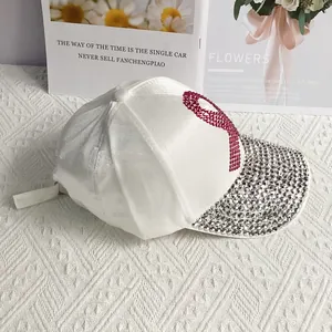 Close-up of white satin baseball cap with rhinestone brim and pink ribbon detail