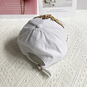 Detail of white baseball cap back featuring adjustable strap and gold lace trim decor