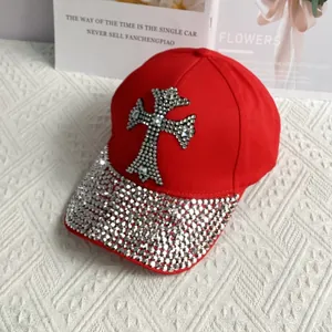 Close-up of red denim baseball cap with silver rhinestone cross and studded brim detail