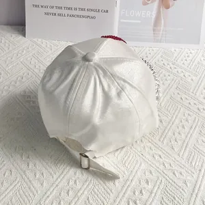 Detail of white satin baseball cap with red rhinestones and adjustable metal buckle