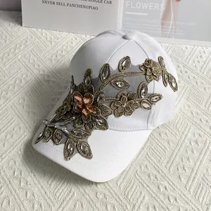 Detail der goldfarbenen Blumenstickerei und glitzernden Strasssteine auf weißer Baseballkappe