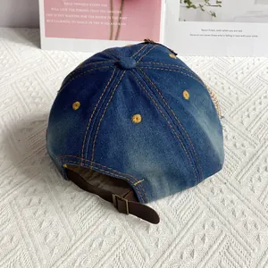Detail of blue denim baseball cap with yellow embroidered dots and brown leather strap