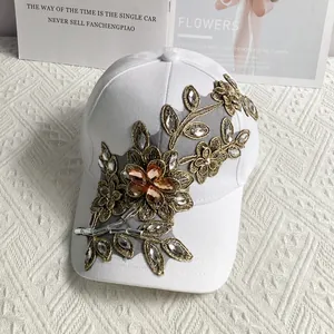 Makroaufnahme einer weißen Baseballkappe mit goldener Blumenstickerei und bernsteinfarbenen Steinen