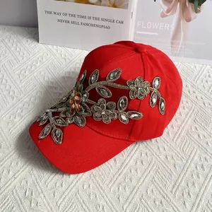 Detail der roten Baseballkappe mit goldenen Blumenstickereien und Glitzersteinen