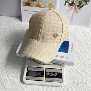 Detailed view of lightweight houndstooth baseball cap with gold M logo on weighing scale