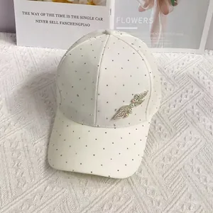 Detailed view of white baseball cap featuring sparkling rhinestones and metal wing decor