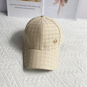 Detail of beige houndstooth baseball cap with golden metal logo on textured fabric