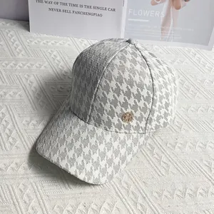 Detail of light grey houndstooth baseball cap with a diamond-studded M-badge logo