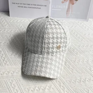 Detailed view of houndstooth baseball cap with gold metal accent and woven fabric texture