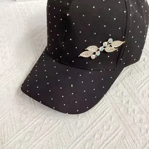 Detail of a black baseball cap featuring silver rhinestones and a sparkling leaf brooch