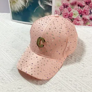 Dettaglio di un cappello da baseball rosa con strass e logo C in metallo dorato di lusso