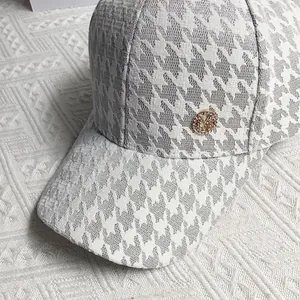 Close-up of golden M logo badge on houndstooth pattern baseball cap detail