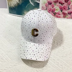 Dettaglio cappello bianco con strass brillanti e logo C in metallo dorato su fondo a maglia