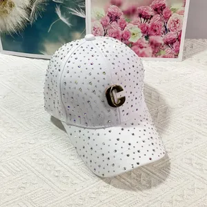 Dettaglio del cappello bianco con strass luccicanti e logo C in metallo dorato